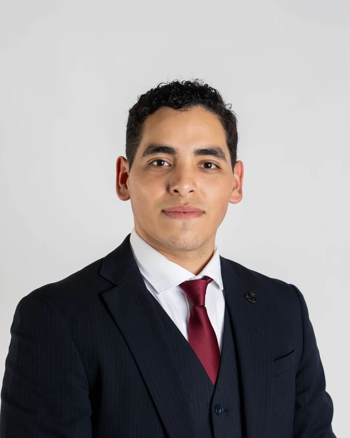 Portrait of Jazer Torres wearing a navy pinstripe suit and a burgundy tie